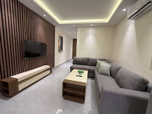 Ein modernes Wohnzimmer mit Flachbildfernseher, grauem Sofa, Holz-Couchtisch und einer eingebauten Bank.