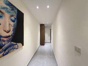 Ein Korridor mit Marmorboden, einer Holztür am Ende und einem großen abstrakten Gemälde an der linken Wand.