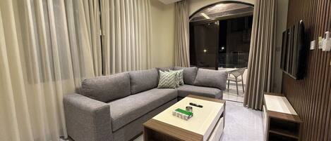 A modern living room with a grey sofa, a wooden coffee table, and a TV mounted on the wall.