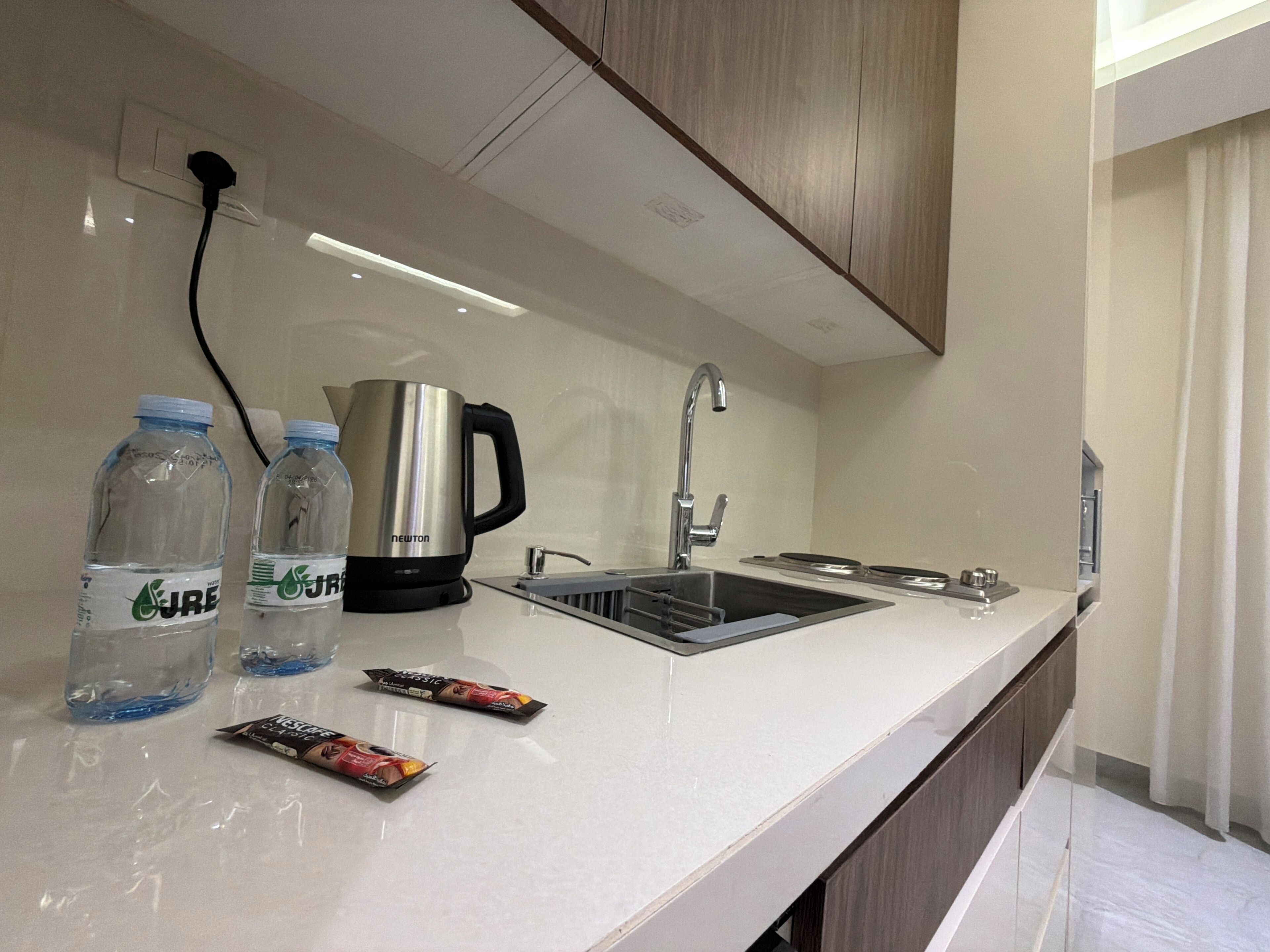 A modern kitchen with a stainless steel sink, a kettle, and bottled water.