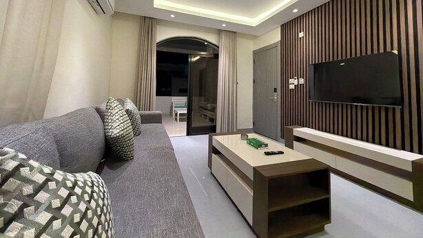 A modern living room with a sofa, a coffee table, a flat-screen TV, and a wall-mounted TV. - 301 JRE 2Bedr rooftop with beautiful view (Amman)