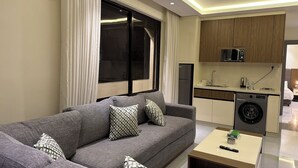 Ein modernes Wohnzimmer mit einem grauen Sofa, gemusterten Kissen, einem Couchtisch und einer integrierten Waschmaschine.