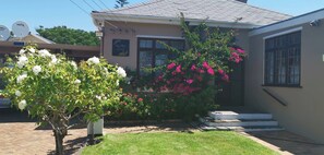 Una casa con antena parabólica, un letrero que dice 'Jive's Place' y un pequeño jardín con flores.