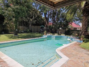 Una piscina con agua cristalina, rodeada por una terraza de piedra y una zona ajardinada con árboles.