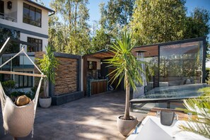 A modern outdoor patio with a glass table, a hanging chair, and potted plants. - La Casita de Luna Bolivia (Sucre)