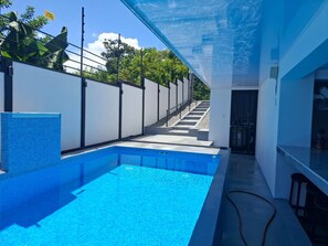 A modern indoor swimming pool with a clear view of the outside, a white wall, and a staircase leading outside.