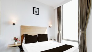 Habitación de hotel con una cama grande, una mesita de noche con lámpara, un cuadro en la pared y una ventana con cortinas.
