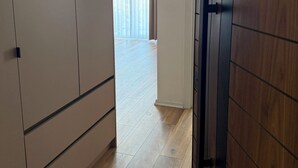 Ein Flur mit einer Holztür, einem Kleiderschrank und Blick in einen Raum mit großem Fenster und Vorhängen.