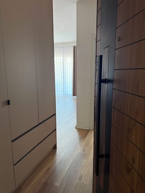 A hallway with a wooden door, a wardrobe, and a view into a room with a large window and curtains. - PineaMare Apartaments Golem, Durres (Golem)