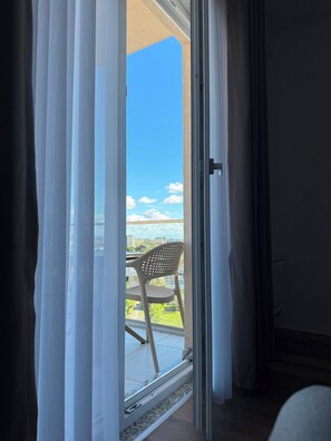 A room with a sliding glass door leading to an outdoor area with a chair and a view of buildings. - PineaMare Apartaments Golem, Durres (Golem)