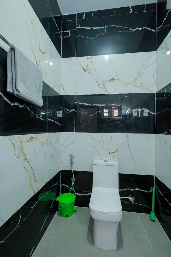 Un baño con un inodoro, cubos verdes y una herramienta de limpieza verde.