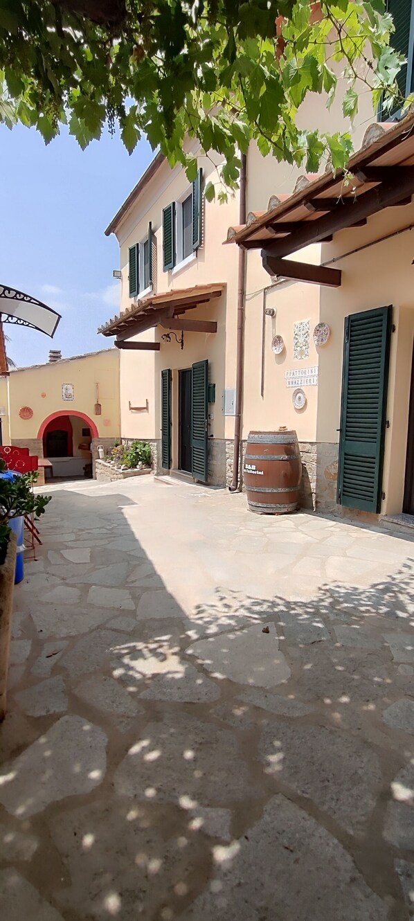 A courtyard with stone flooring, a barrel, and a building with green shutters.