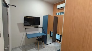 Habitació petita amb escriptori, televisió i un mur compartit.