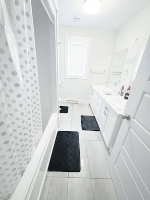 A bathroom with a white door, a white sink, a mirror, and a black mat on the floor. - Modern 3-bedroom Retreat Near Moncton Hospital and Downtown (Moncton)