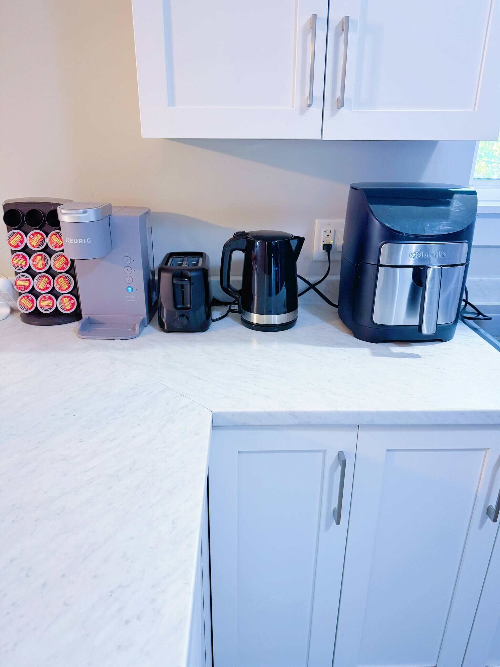 Cozinha equipada com máquina de café, torradeira, chaleira e cápsulas de café.