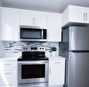 A modern kitchen with white cabinets, a stainless steel microwave, oven, and refrigerator. - Modern 3-bedroom Retreat Near Moncton Hospital and Downtown (Moncton)