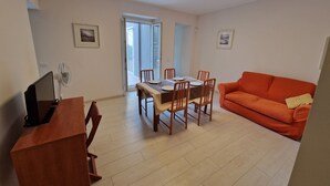Un salon comprenant une table à manger, un canapé orange et un téléviseur posé sur un meuble en bois.