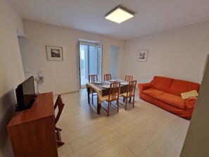 A living room with a dining table, orange sofa, and a TV on a wooden stand. - Apartments Villa Fulgida Ground Floor (Cattolica)