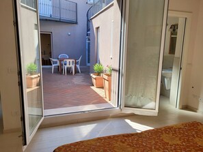A room with a sliding glass door leading to an outdoor patio with a table and chairs, potted plants, and a view of a building with a balcony. - Apartments Villa Fulgida Ground Floor (Cattolica)
