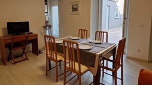 Un coin repas avec une table dressée pour quatre personnes, un téléviseur posé sur un bureau et une vue sur l’extérieur par une porte.