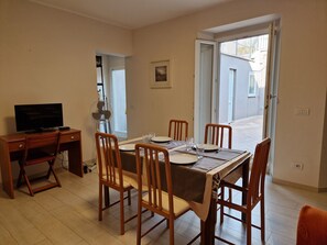 A dining area with a table set for four, a television on a desk, and a view of the outside through a door. - Apartments Villa Fulgida Ground Floor (Cattolica)