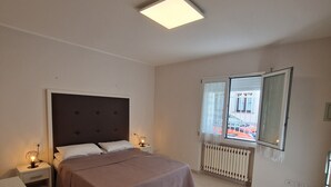 Une chambre à coucher comprenant un lit, des tables de chevet, un bureau, une chaise, un radiateur et une fenêtre donnant sur un paysage agréable.