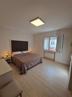 A bedroom with a bed, bedside tables, a desk, a chair, a radiator, and a window with a view. - Apartments Villa Fulgida Ground Floor (Cattolica)