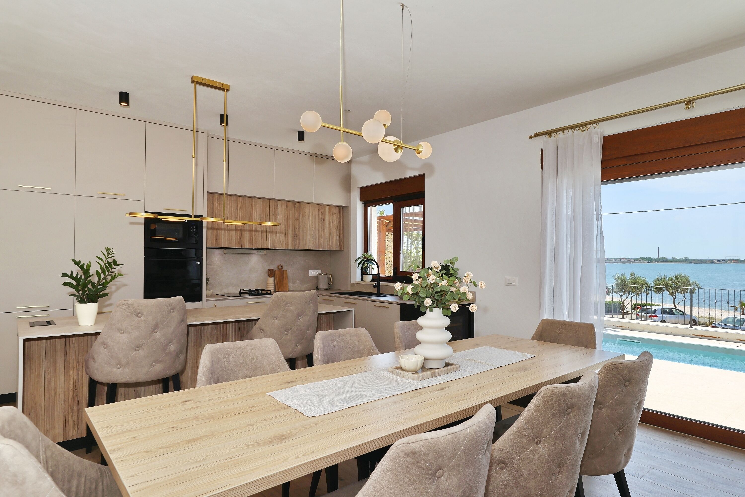 A modern kitchen with a dining area, a view of the sea, and a pool.