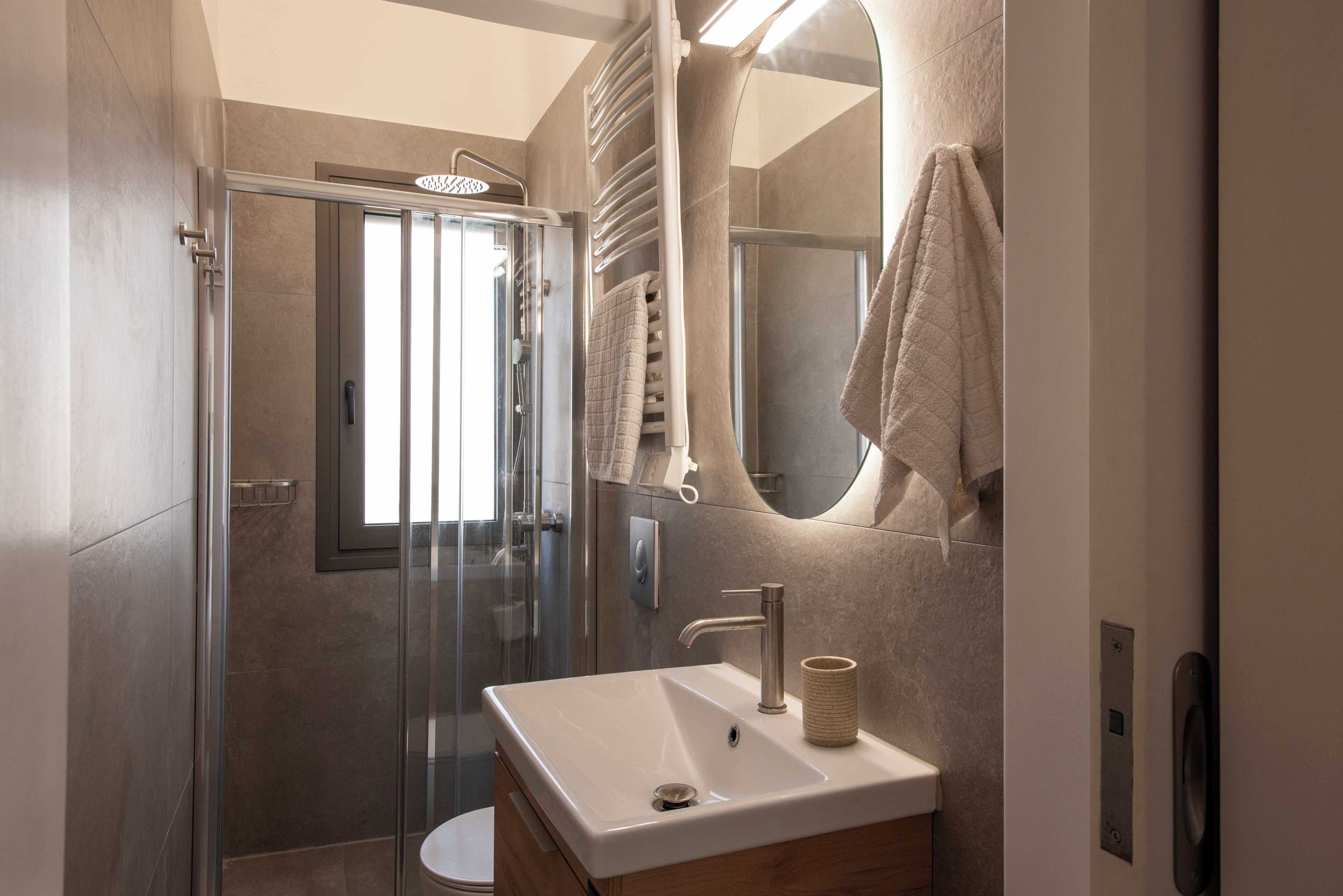 Ein modernes Badezimmer mit einer Duschkabine aus Glas, einem weißen Waschbecken und einem Spiegel mit aufgehängtem Handtuch.