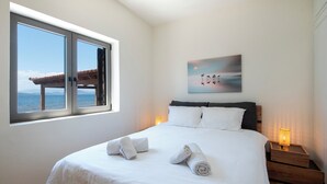Ein Schlafzimmer mit großem Fenster, einem Bett mit weißer Bettwäsche, zwei Nachttischlampen und einem Gemälde an der Wand.