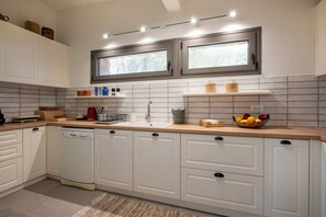 A modern kitchen with white cabinetry, a dishwasher, a sink, and a window above the countertop. - Villa Isabelle on the beach (Iria)