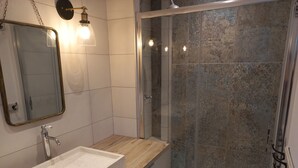 Ein modernes Badezimmer mit Duschkabine aus Glas, einem Waschbecken mit Holzauskładung und einem Spiegel mit goldener Rahmung.