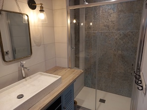 Ein modernes Badezimmer mit Duschkabine aus Glas, einem Waschbecken mit Holzauskładung und einem Spiegel mit goldener Rahmung.