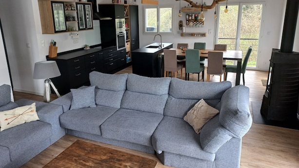 Ein modernes Wohnzimmer mit grauem Sofa, Holz-Couchtisch und einem Essbereich mit Stühlen und Tisch.