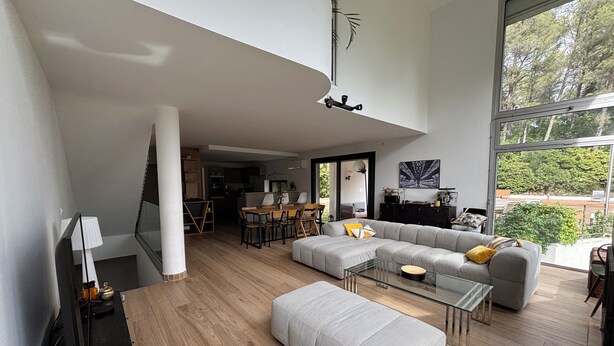 Ein modernes Wohnzimmer mit einer Eckcouch, einem Hocker, einem Glastisch und einem Essbereich mit Stühlen.