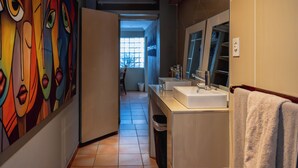 Ein modernes Badezimmer mit einem großen Spiegel, zwei Waschbecken und einem farbenfrohen, abstrakten Wandbild.