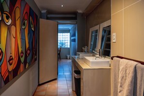 Et moderne badeværelse med et stort spejl, to håndvaske og et farverigt abstrakt mural på væggen.