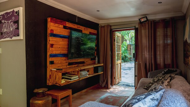 Ein Wohnzimmer mit einem TV-Schrank aus Holz, einer Couch, einem kleinen Tisch und einem großen Fenster mit Vorhängen.