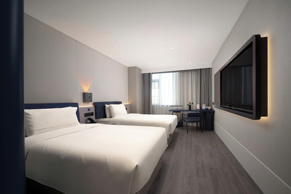 Habitación de hotel con dos camas, un escritorio, una silla, un televisor y una ventana con cortinas.