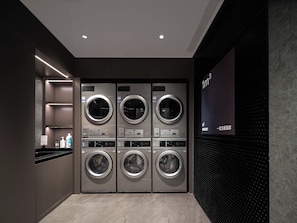 A modern laundry facility with four front-loading washing machines, a digital display, and a tiled floor. - North Bund Light Stay Hotel Shanghai (Shanghai)
