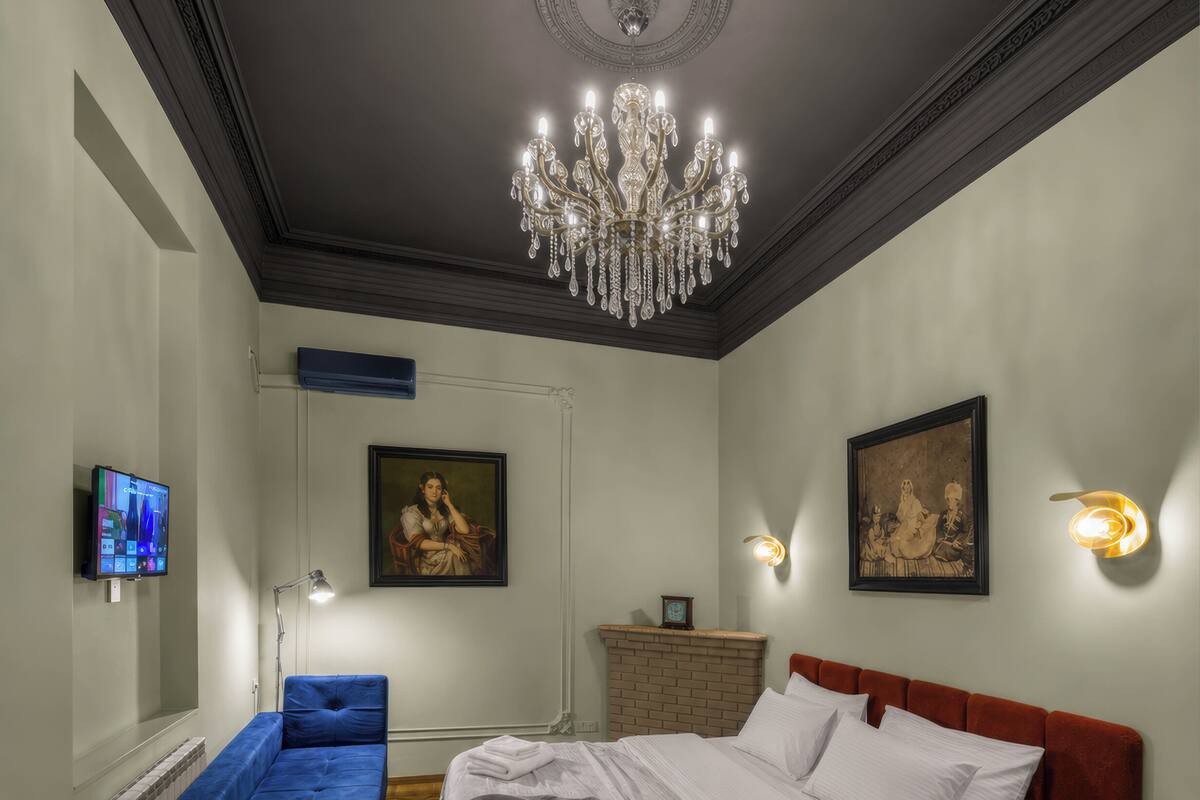 A bedroom with a large bed, a blue sofa, a chandelier, and artwork on the walls.