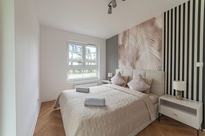 A bedroom with a bed, a nightstand, a lamp, a window, and a wall with a striped pattern.