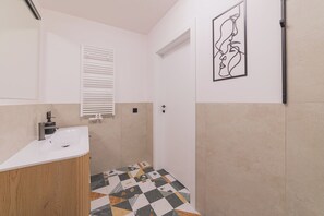 A bathroom with a white sink, a wooden vanity, a tiled floor, a white door, and a wall-mounted abstract art piece.