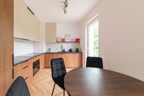 Una cocina moderna con armarios de madera, encimera negra y zona de comedor con mesa de madera oscura y sillas negras.