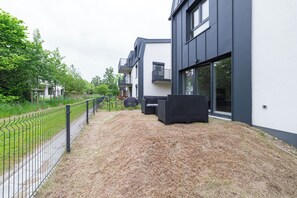 Ein modernes Gebäude mit flachem Dach, großen Fenstern und einer gepflasterten Fläche mit Gartenmöbeln.