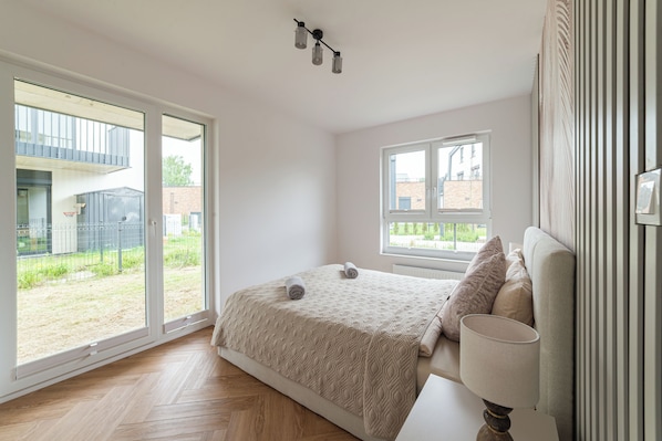 A bedroom with a bed, a window, a lamp, and a view of the outside.