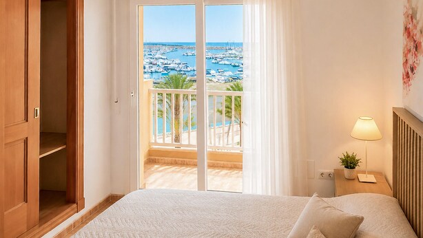 Habitación de hotel con cama, mesita de noche, lámpara, vista hacia un puerto deportivo y un armario de madera.