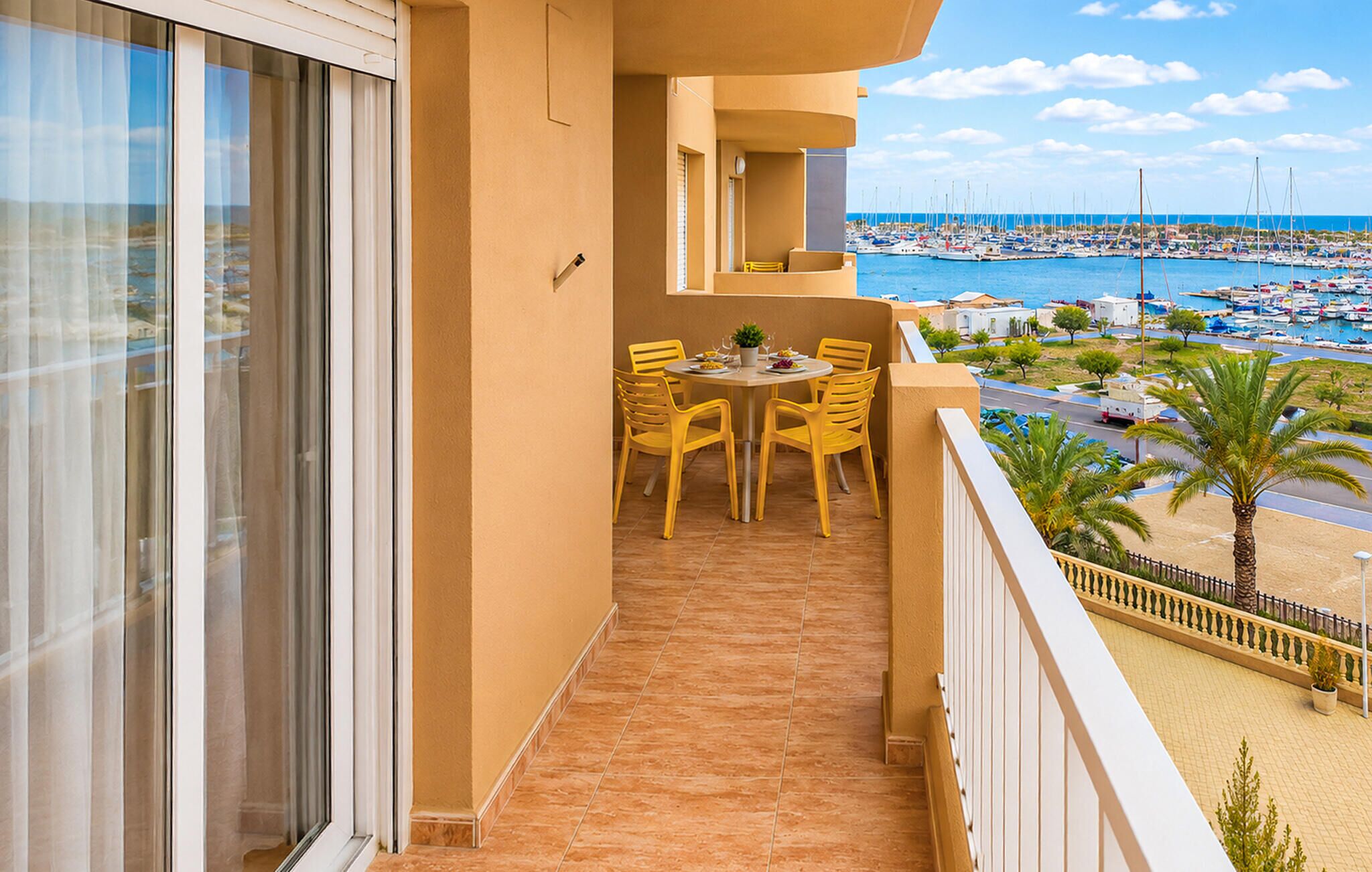 Un balcon avec une table et des chaises, donnant sur une marina où sont amarrés des bateaux.