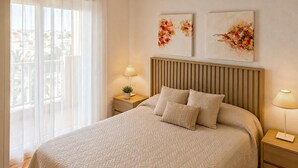 Una cama bien hecha con una colcha estampada, dos almohadas, una mesita de noche con una lámpara y dos obras de arte colgadas en la pared.