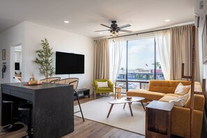 Ett modernt vardagsrum med en stor TV, en soffa, en matplats och utsikt över staden.